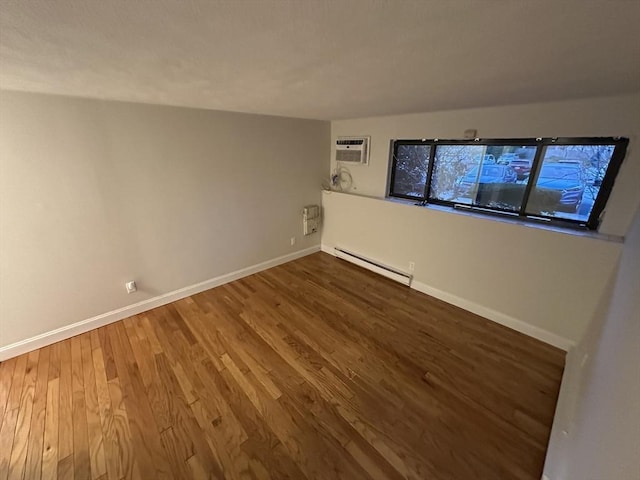 spare room with baseboards, a baseboard heating unit, a wall unit AC, and wood finished floors