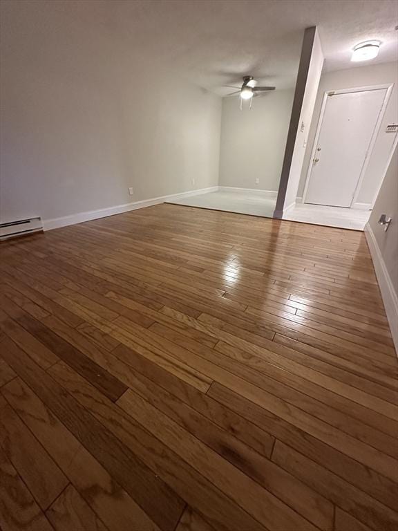 empty room featuring a baseboard heating unit, ceiling fan, dark wood finished floors, and baseboards