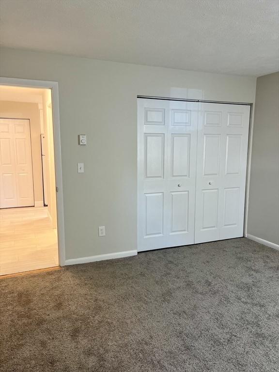 unfurnished bedroom with carpet floors, a textured ceiling, baseboards, and a closet