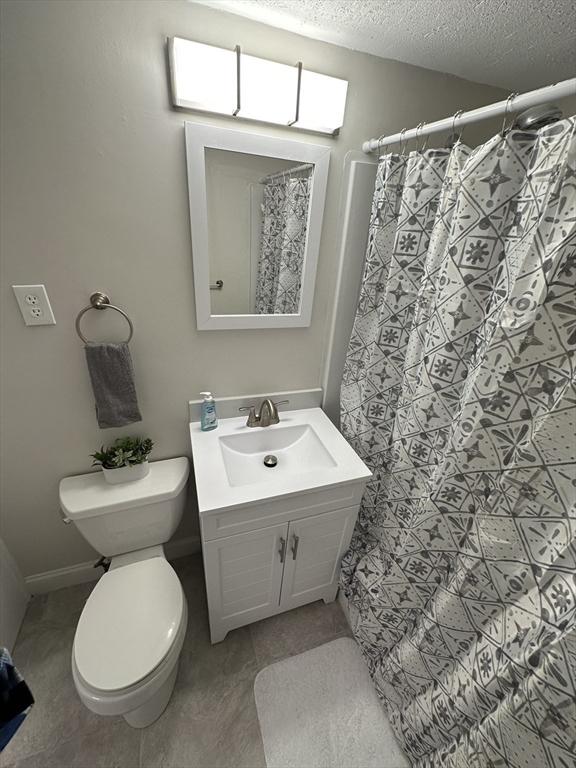 full bath with a textured ceiling, tile patterned flooring, curtained shower, vanity, and toilet