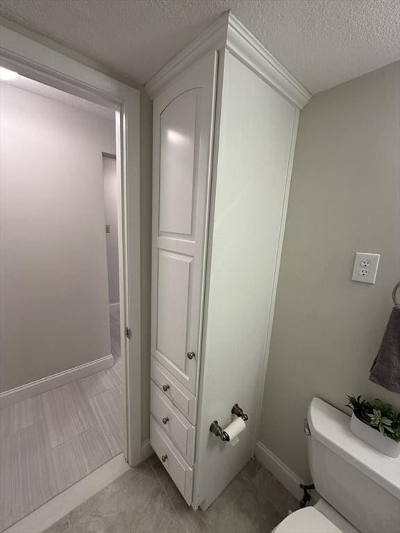 bathroom with baseboards, a textured ceiling, tile patterned flooring, and toilet