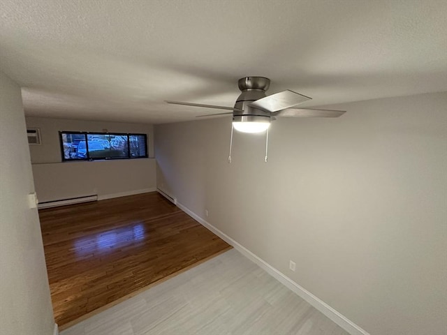 spare room with a baseboard radiator, a ceiling fan, baseboards, light wood-type flooring, and a baseboard heating unit