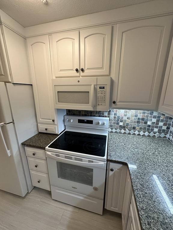 kitchen with white appliances, white cabinetry, decorative backsplash, and dark stone countertops