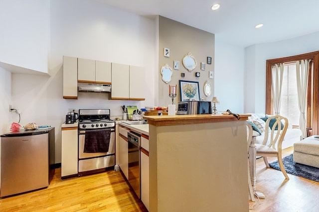 kitchen with appliances with stainless steel finishes, light hardwood / wood-style floors, and kitchen peninsula