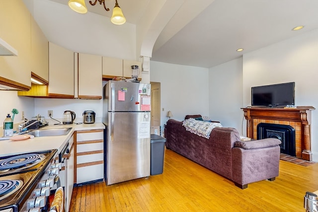 kitchen with a tile fireplace, light hardwood / wood-style flooring, stainless steel appliances, sink, and cream cabinetry