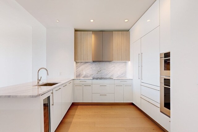 kitchen featuring sink, kitchen peninsula, decorative backsplash, black electric stovetop, and light wood-type flooring