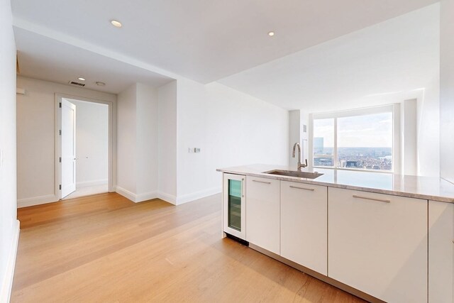 kitchen with light hardwood / wood-style floors, white cabinetry, sink, and beverage cooler