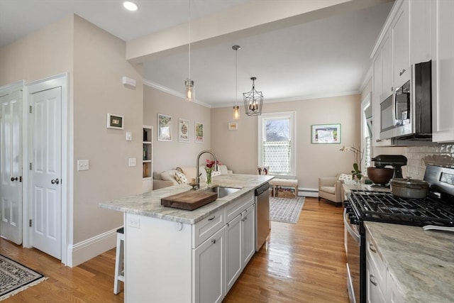 kitchen with an island with sink, appliances with stainless steel finishes, pendant lighting, and white cabinets