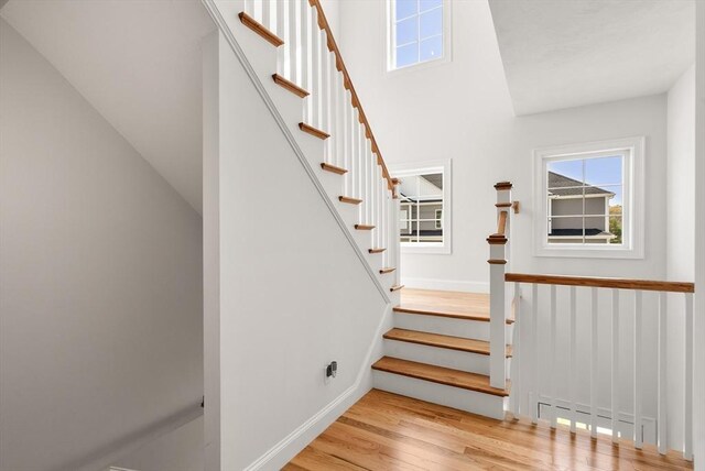 stairway with baseboards, wood finished floors, and a healthy amount of sunlight