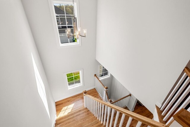 stairway featuring baseboards, a high ceiling, wood finished floors, and a chandelier