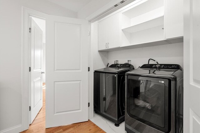 washroom with cabinet space, separate washer and dryer, and light wood-style flooring