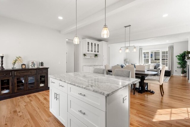 kitchen featuring white cabinets, light wood-type flooring, a kitchen island, beamed ceiling, and pendant lighting