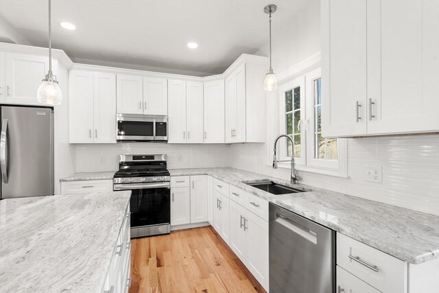 kitchen featuring light stone counters, a sink, stainless steel appliances, white cabinetry, and backsplash
