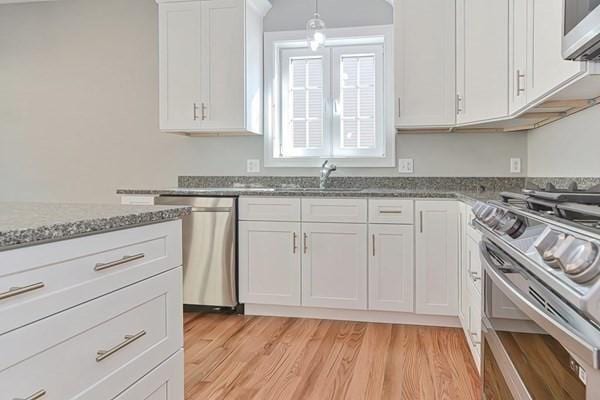 kitchen with white cabinetry, decorative light fixtures, appliances with stainless steel finishes, stone counters, and light hardwood / wood-style floors