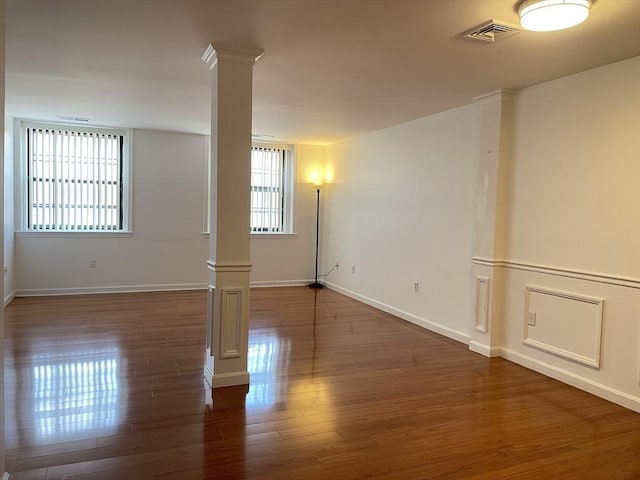 unfurnished room featuring ornate columns, wood finished floors, and baseboards