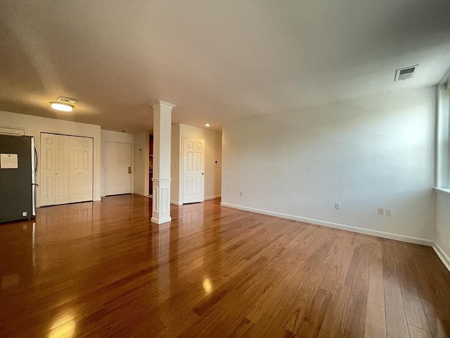 spare room featuring decorative columns, wood finished floors, and baseboards