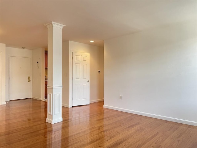 empty room featuring decorative columns, light wood-type flooring, baseboards, and recessed lighting