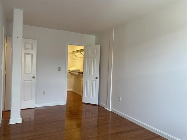 unfurnished bedroom featuring wood finished floors, baseboards, a spacious closet, and a closet