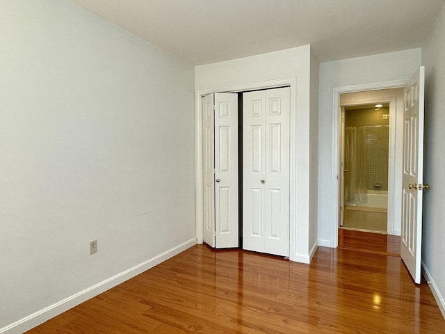 unfurnished bedroom with wood finished floors, baseboards, and a closet