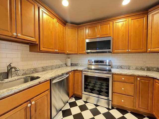 kitchen featuring appliances with stainless steel finishes, light flooring, a sink, backsplash, and light stone counters