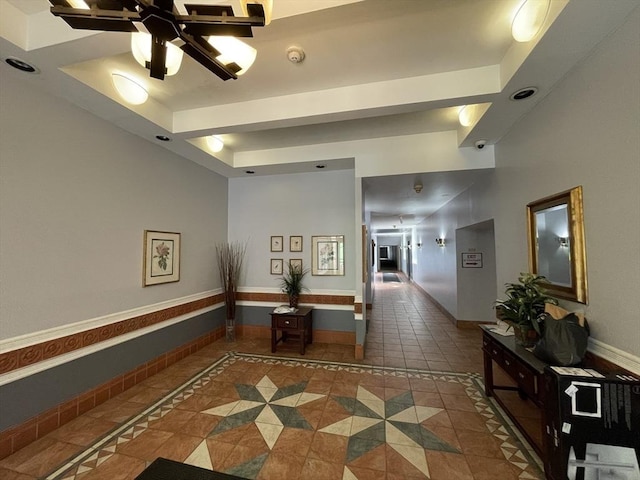 hallway with a raised ceiling, inlaid floor details, tile patterned floors, and baseboards