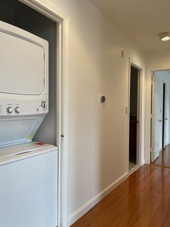 laundry area featuring stacked washer and clothes dryer, wood finished floors, and baseboards