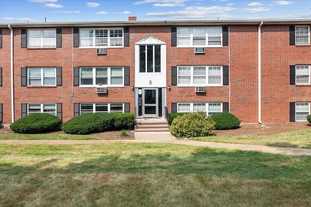 view of front of home featuring a wall unit AC and a front lawn