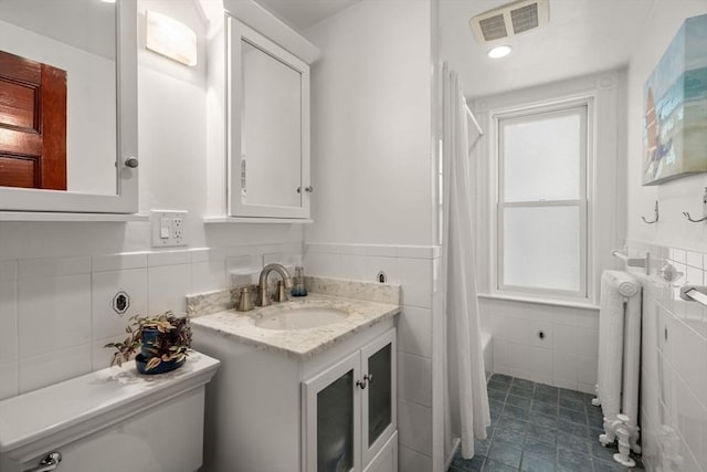 bathroom with visible vents, tile walls, toilet, radiator heating unit, and vanity