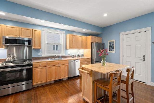 kitchen featuring dark wood finished floors, light brown cabinetry, a sink, appliances with stainless steel finishes, and a kitchen bar