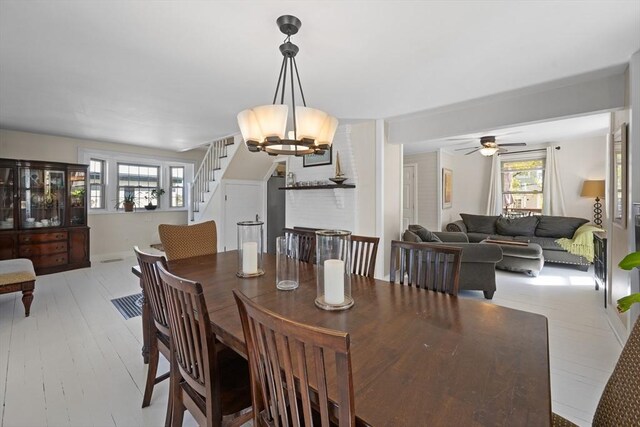 dining room with stairway, ceiling fan with notable chandelier, light wood finished floors, and a healthy amount of sunlight