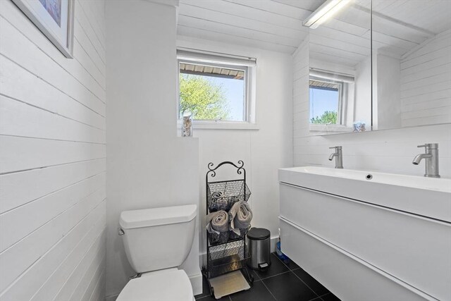 bathroom featuring vanity, tile patterned flooring, wood walls, and toilet