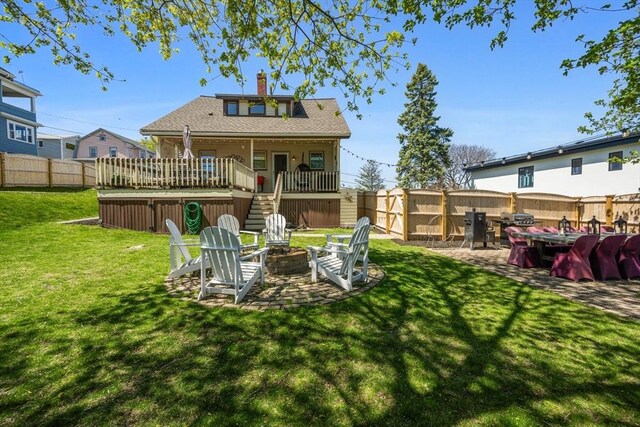 rear view of house featuring an outdoor fire pit, a wooden deck, a fenced backyard, a chimney, and a yard