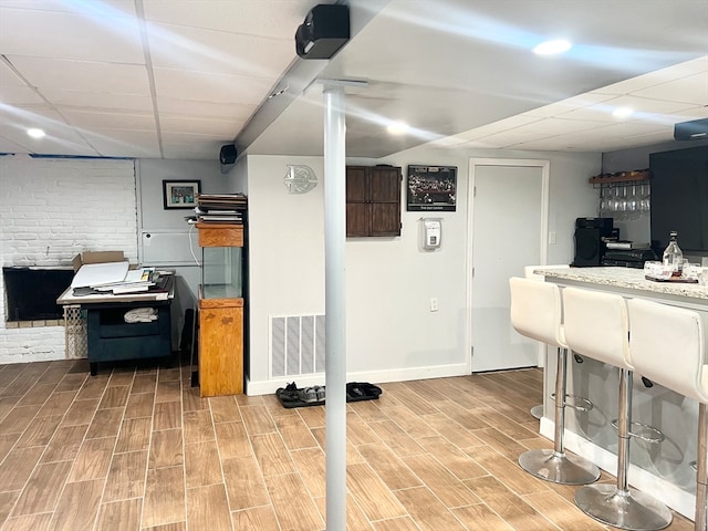 basement with light hardwood / wood-style floors, brick wall, and a paneled ceiling