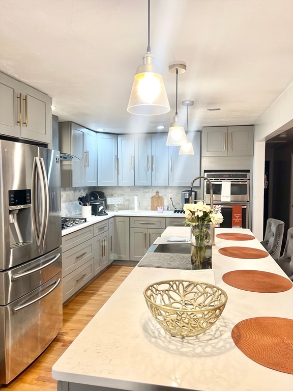 kitchen with tasteful backsplash, light stone countertops, light hardwood / wood-style floors, stainless steel appliances, and decorative light fixtures