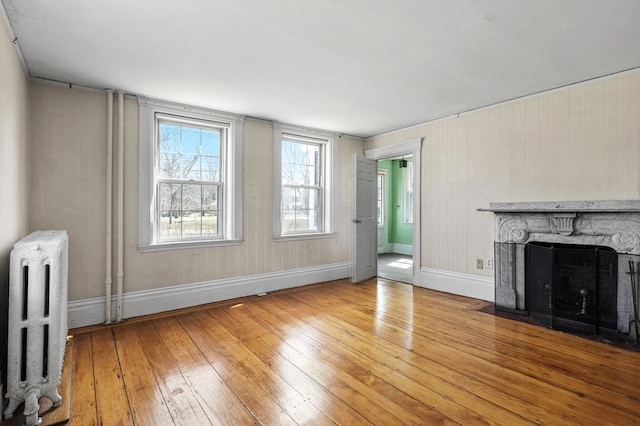 unfurnished living room with radiator, light wood-type flooring, baseboards, and a fireplace with flush hearth