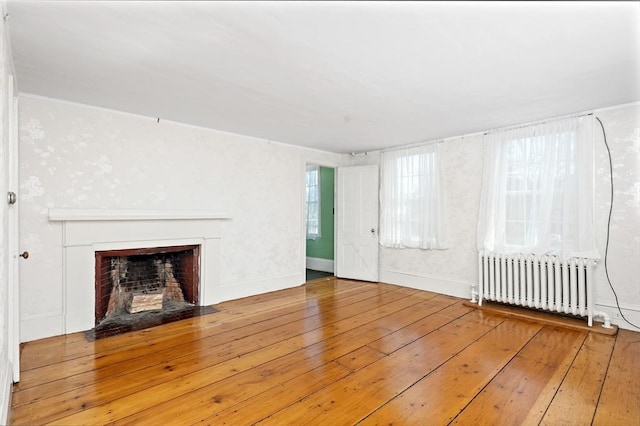 unfurnished living room with hardwood / wood-style flooring, a fireplace with flush hearth, baseboards, and radiator heating unit