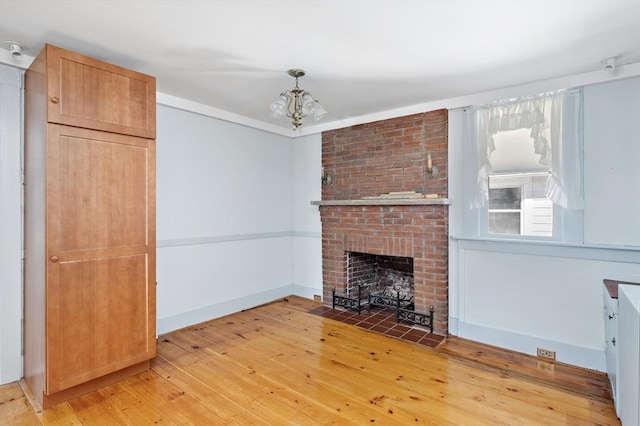 unfurnished living room with light wood-type flooring, a brick fireplace, an inviting chandelier, and crown molding