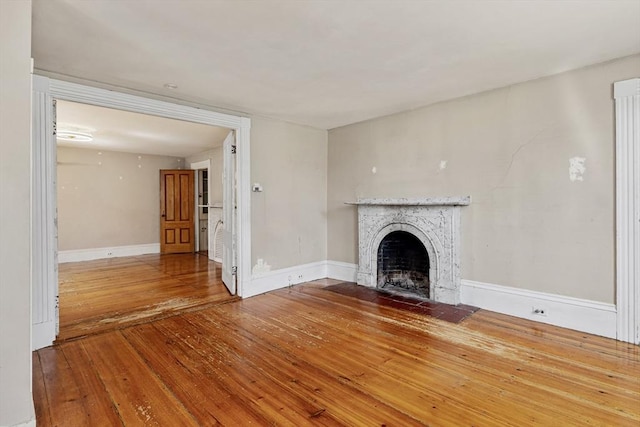 unfurnished living room featuring a tiled fireplace, baseboards, and wood-type flooring