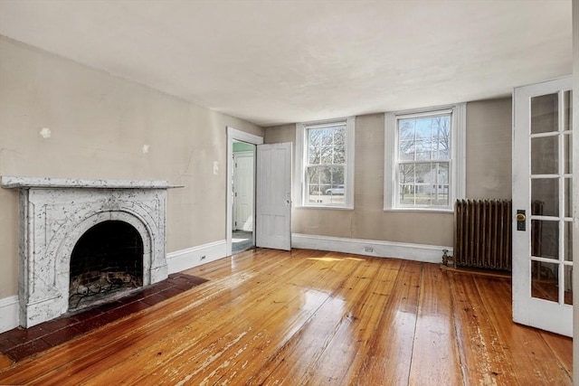 unfurnished living room featuring radiator heating unit, a fireplace, baseboards, and hardwood / wood-style floors