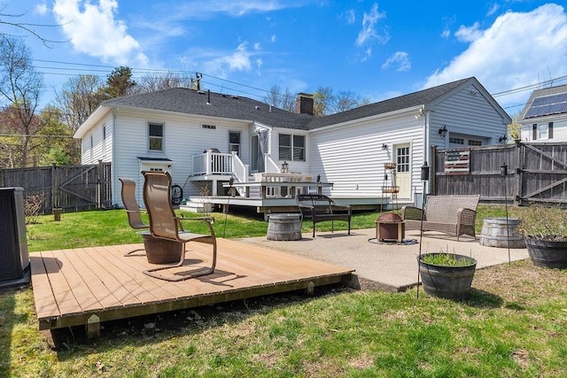 rear view of house featuring a fenced backyard, a gate, a wooden deck, and a fire pit