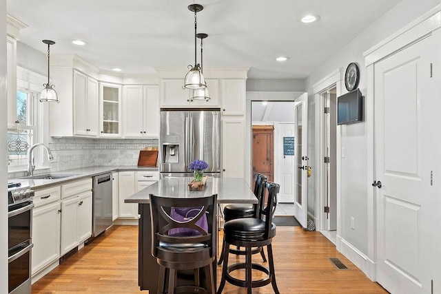 kitchen featuring decorative backsplash, a sink, glass insert cabinets, stainless steel appliances, and white cabinetry