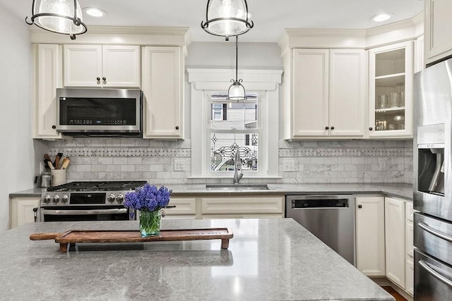 kitchen featuring hanging light fixtures, light stone counters, a sink, stainless steel appliances, and glass insert cabinets