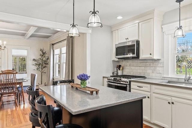 kitchen with white cabinets, appliances with stainless steel finishes, a sink, tasteful backsplash, and a kitchen island