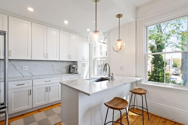 kitchen featuring backsplash, hanging light fixtures, light hardwood / wood-style floors, light stone counters, and white cabinetry