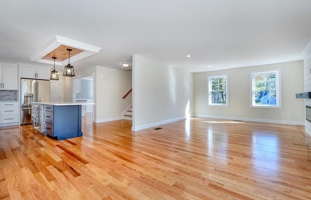 unfurnished living room featuring visible vents, baseboards, stairway, light wood-style flooring, and a glass covered fireplace