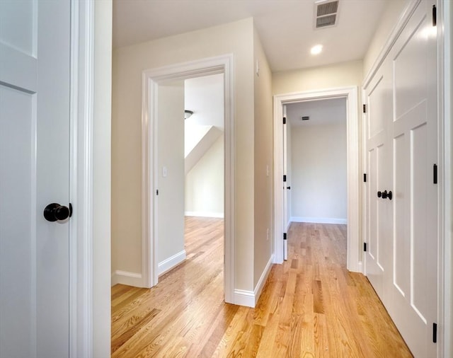 hallway with visible vents, baseboards, and light wood finished floors