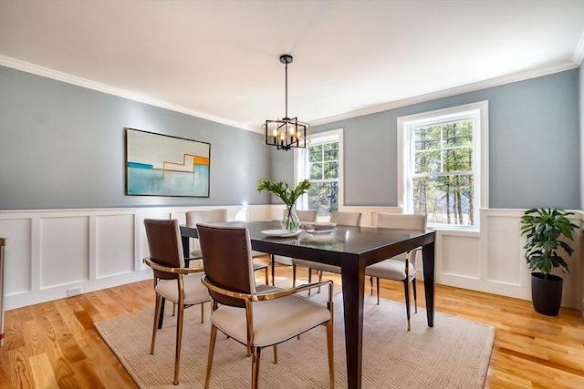 dining area featuring a wainscoted wall, a notable chandelier, ornamental molding, and light wood finished floors