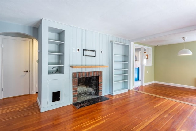 22 Sherman Ave, Northampton, MA 01060 - unfurnished living room with built in shelves, baseboards, wood-type flooring, a brick fireplace, and arched walkways
