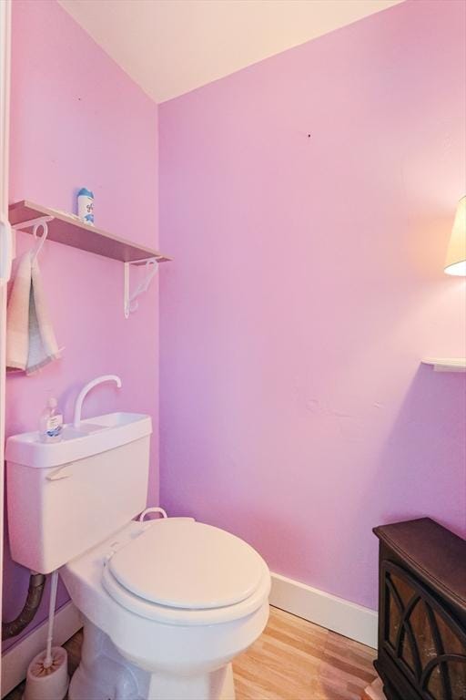 half bath featuring baseboards, toilet, and wood finished floors