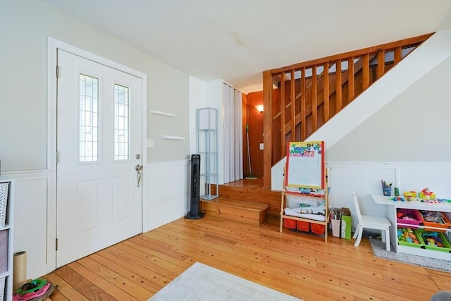 foyer with wood-type flooring, stairs, wainscoting, and a decorative wall